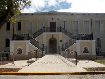 The front of a big building (legislature of the Virgin Islands). It is in a soft yellow colour and white with stairs to the entrance on both sides.