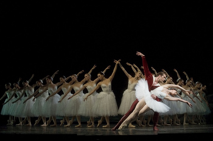 A play with ballerinas wearing white dresses on stage, in the front there are a male and female ballerina dancing together