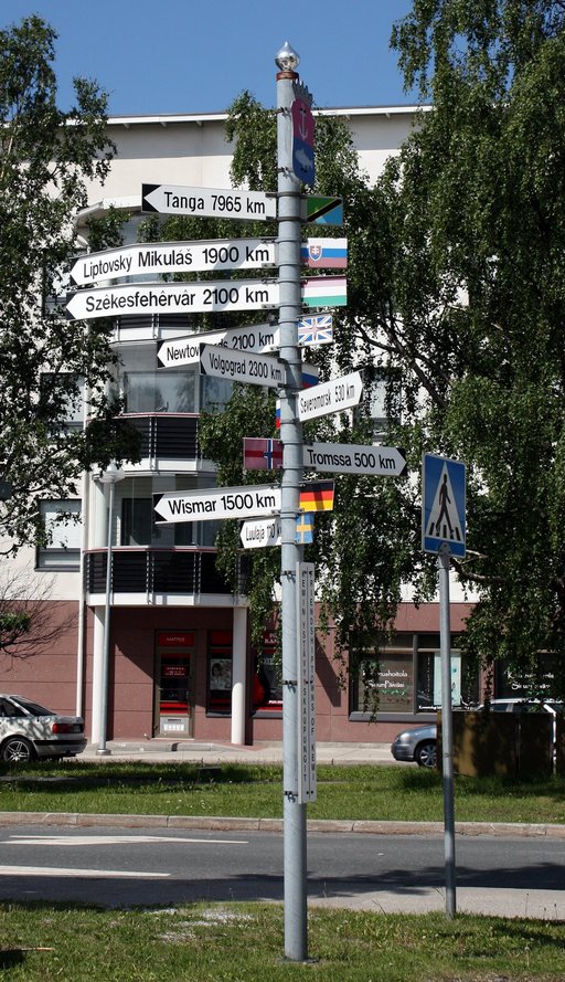A street sign pointing at various cities located in different countries 