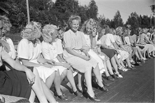 young women sitting beside each other in a line, wearing dresses and skirts