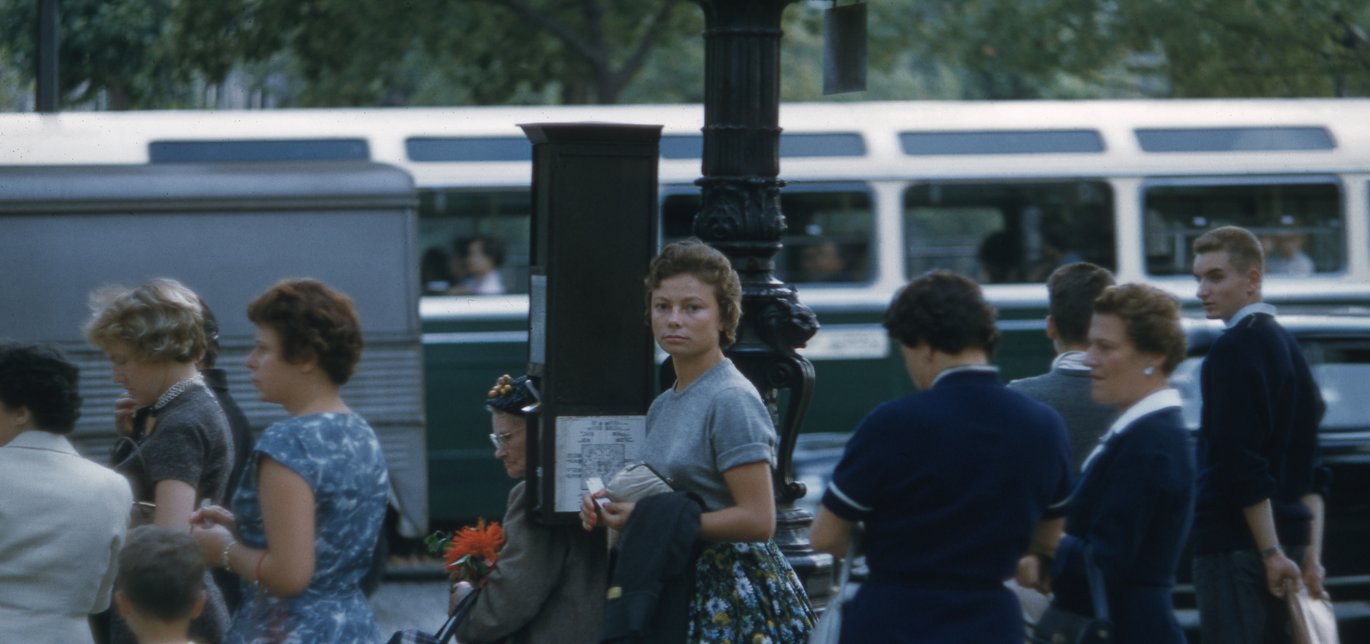 1960s woman looking into camera while waiting for bus to go to work