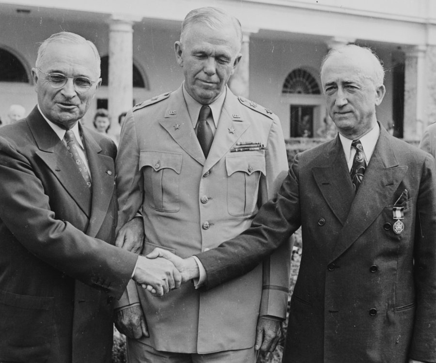 Three men standing side by side, the two the sides are shaking hands.