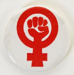 A badge with the logo of feminism. Outlined in red, it shows the gender symbol of a woman with a fist in the centre.