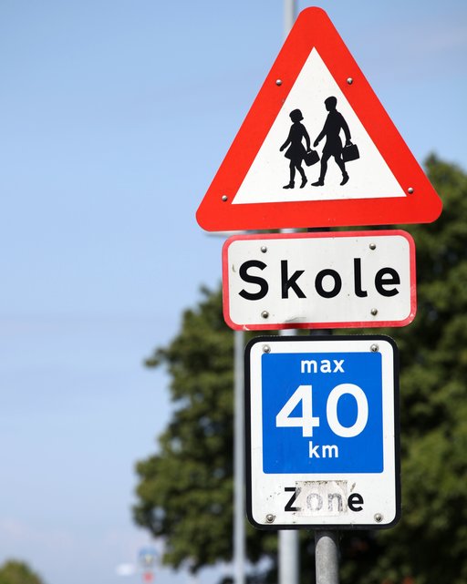 A picture of a triangular traffic sign with red edges. In the white middle are two children with schoolbags. Beneath the sign is a rectangular sign with the Danish word for 'School'. Beneath those two signs is a square sign displaying that the maximum speed in that area is 40 kilometres per hour.