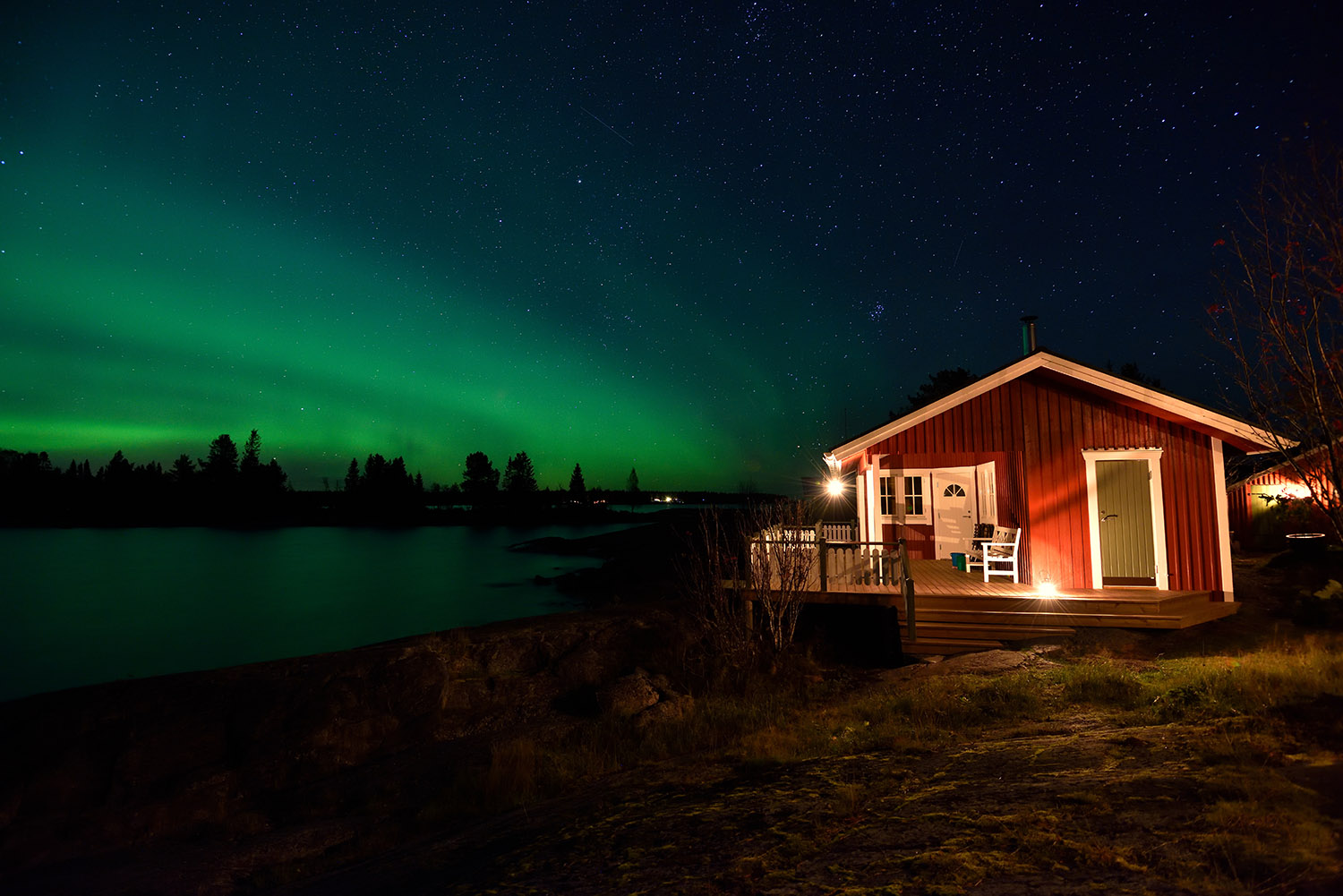 A house by the water, there are green northern lights in the sky