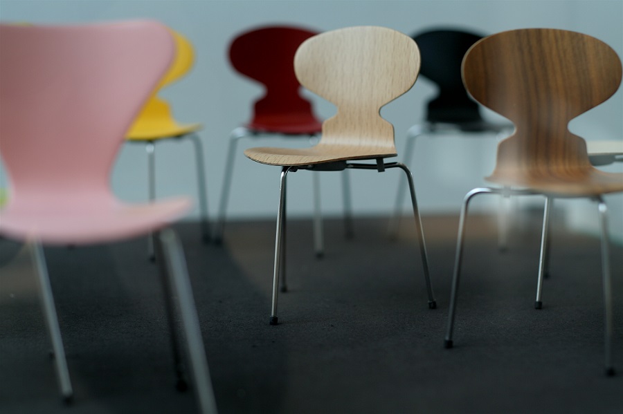 Around six ant chairs, displayed in rows in different colours. They are round at the top and goes in at the hip.