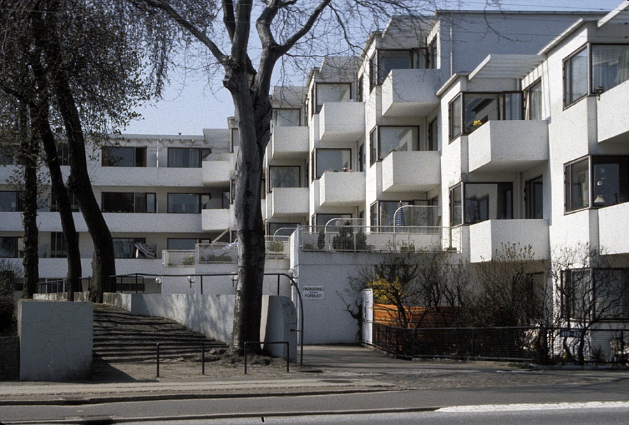 A white apartment complex that is asymmetrical and not straight. Each balcony goes out a bit more than the other.