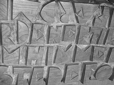Black and white photo of a part of a bench with carved letters in it.