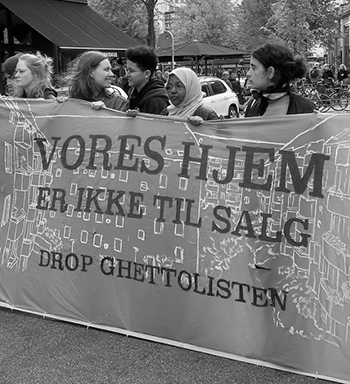Black and white photo of several women holding a banner reading "vores hjem" (our home). The photo is from a demonstration against the so called 'ghetto list', Copenhagen September 2018.