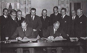 Signing of the The Saltsjöbaden Agreement in 1938. Two men are sitting down and signing while others are standing behind and watching