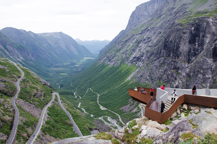 A bird-view from up in the mountains and valleys with small roads here and there. In the corner, you see a lookout where visitors/tourists can stand and look at the view.