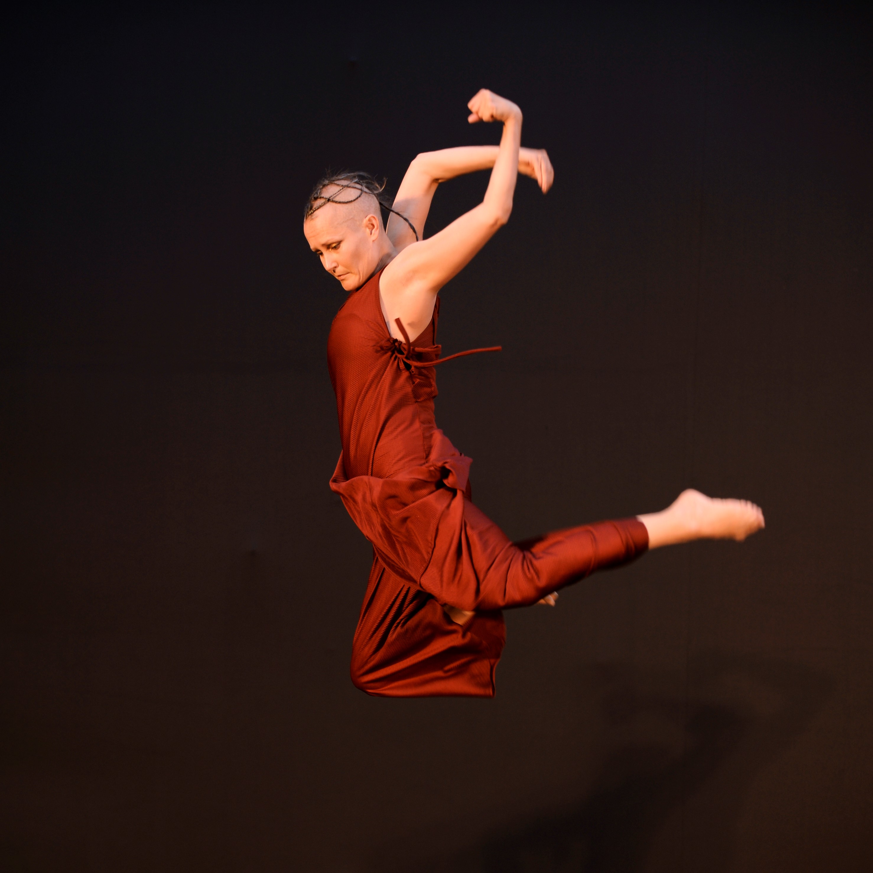 Dancer dressed in maroon silk with arms and legs behind them while they jump in the air