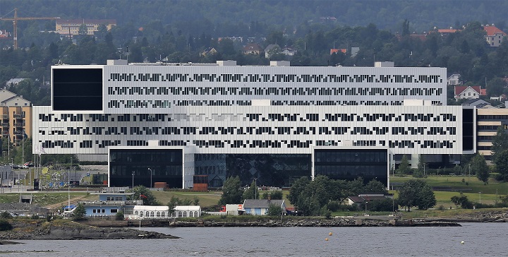 Picture taken from a distance of a very wide black and white building. The building consists of two horisontal rectangular buldings crossed over eachother in an X. 