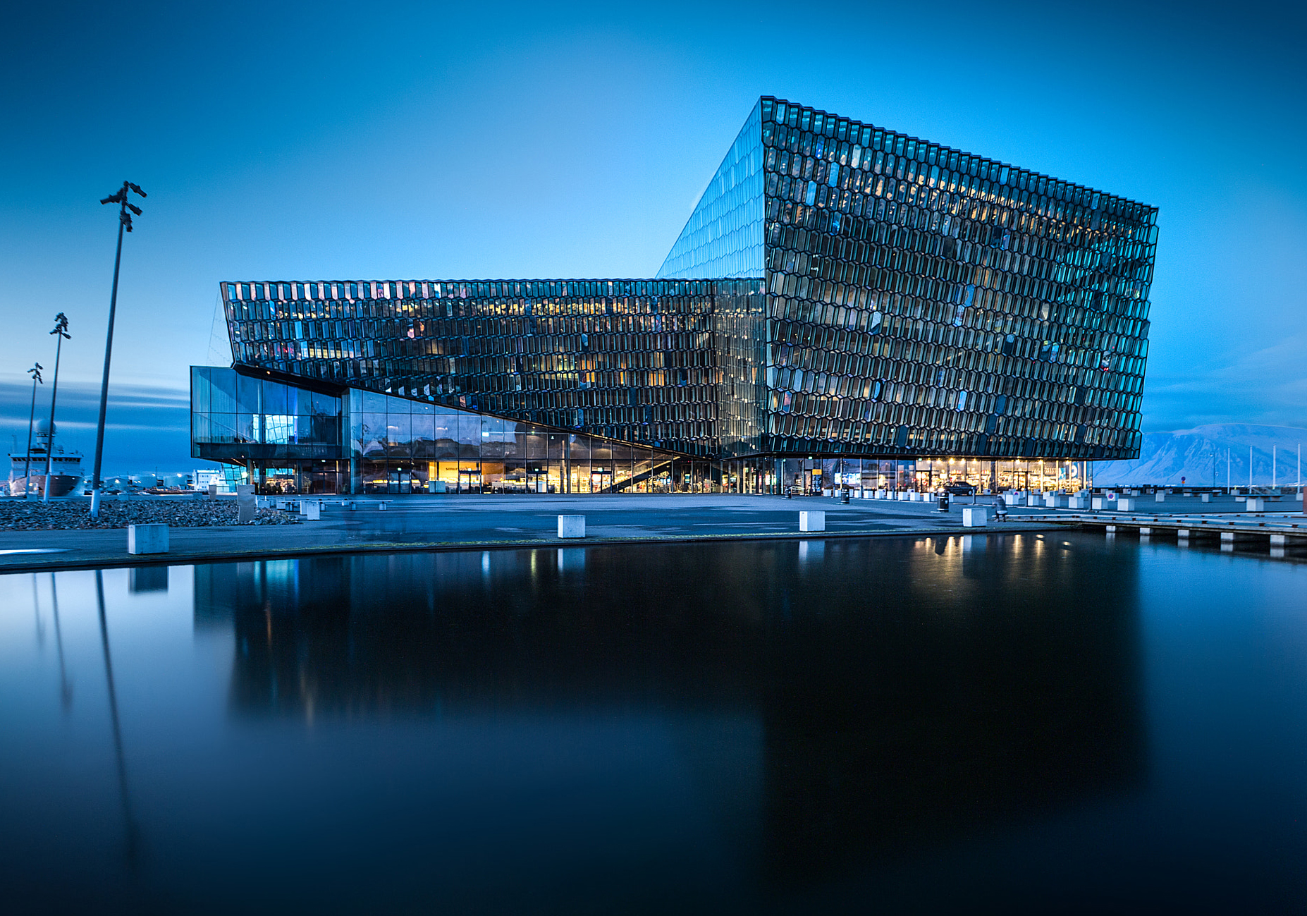 Taken at night. Beautiful evening view of an asymmetric building placed just by the water. In the windows, there are lights.