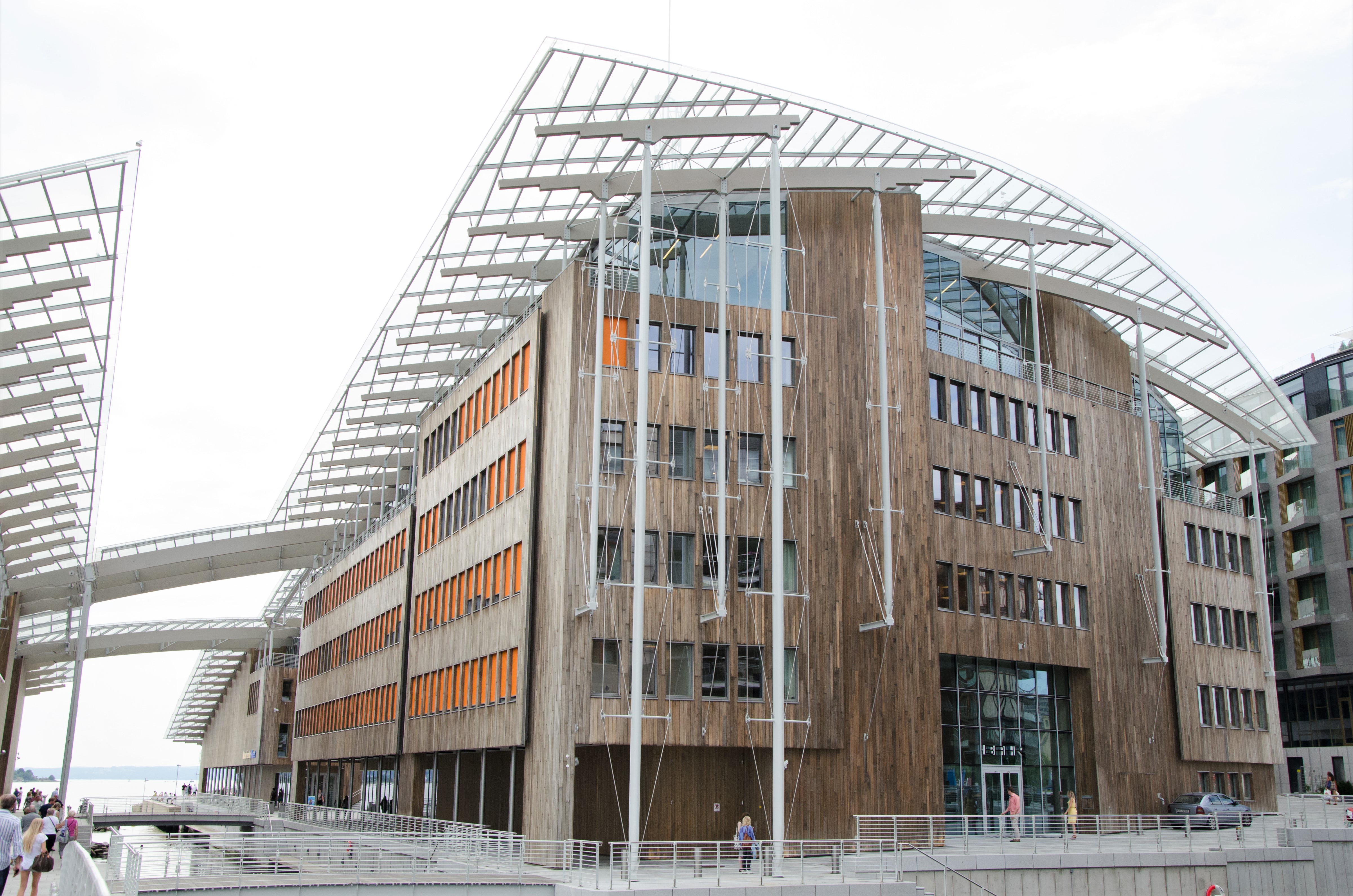 Large building built out of light brown wood. The building's top is roundly shaped and has a fence-looking layer. It is also connected to another similar looking building through two small bridges.