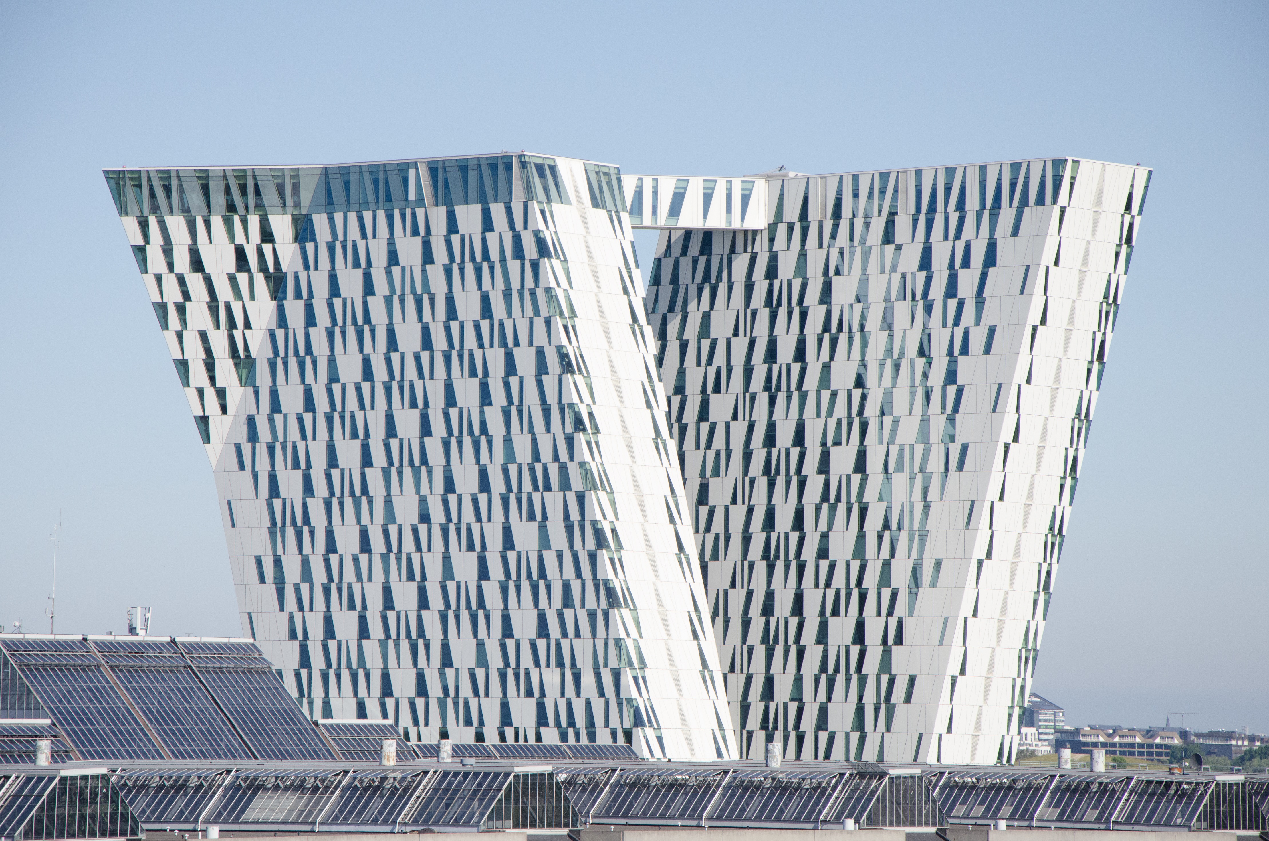 A powerful expressive work with two inclined and faceted towers connected by a sky bridge. The buildings are trapez shaped and made with white plates and glass.