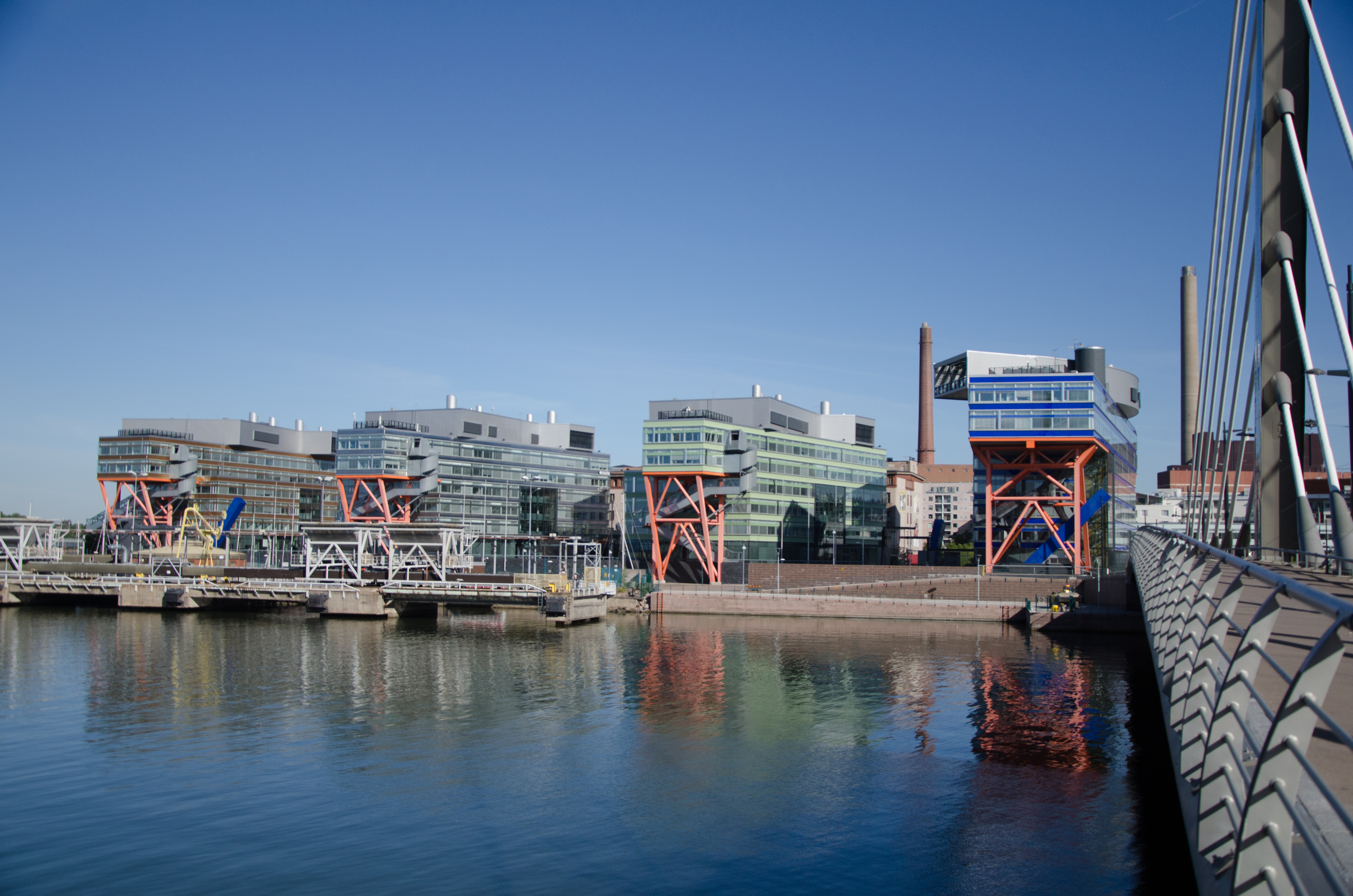 Four buildings covered with glass windows placed right beside each other very close to the habour. They each have a crane-like structure in the front. That means - poles geometrically structured across each other for a strong hold.