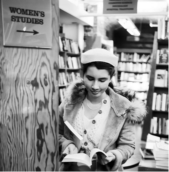 Black and white picture of a young woman reading in the women's studies section ca 1960s.