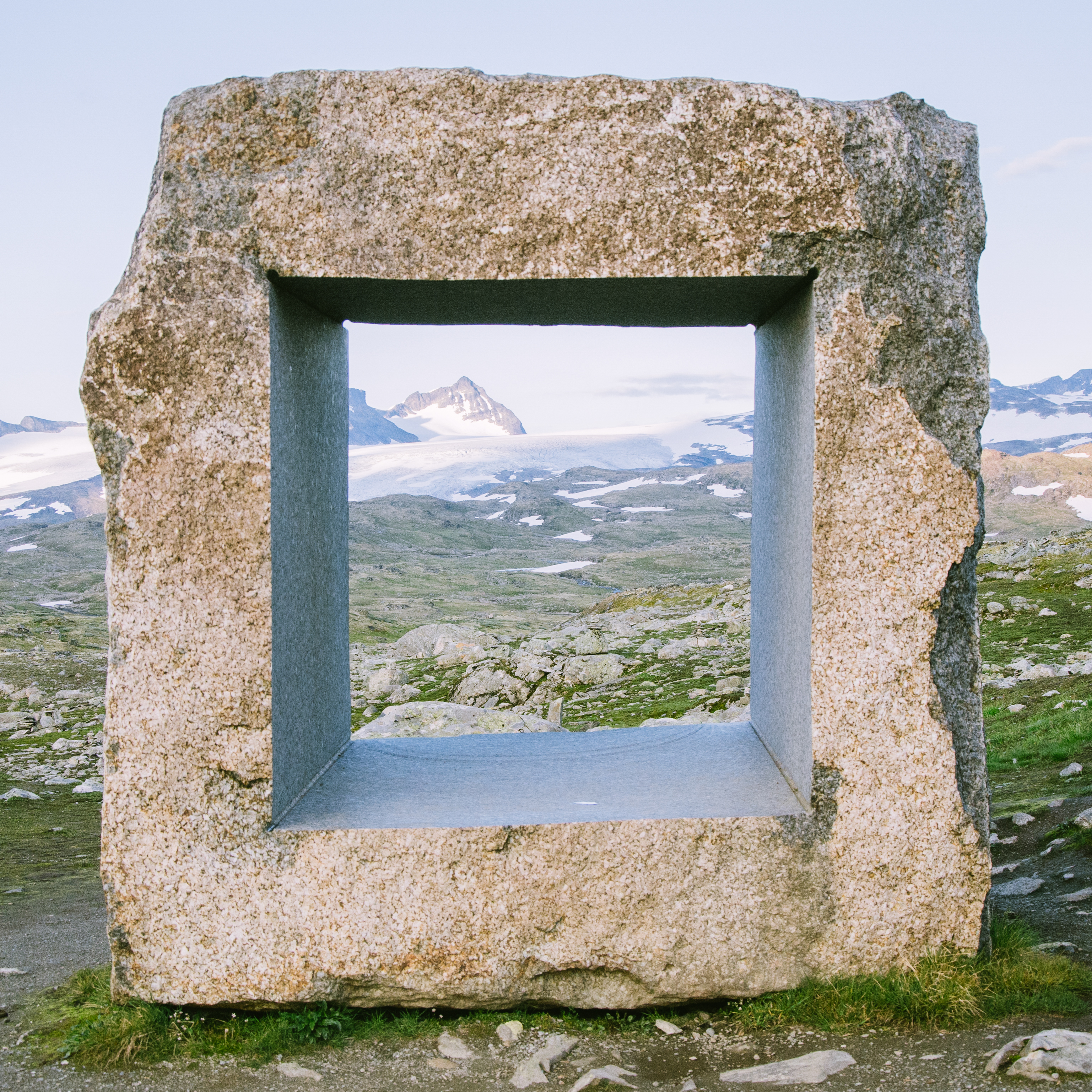 A large square frame made from stone. Its inside edges are perfectly even, while the outside edges are uneven stone. Placed high up in the mountains and hills.