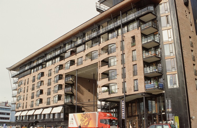 A large building that is part black and part light brown. The balconies on each floor are shaped in 2 ways