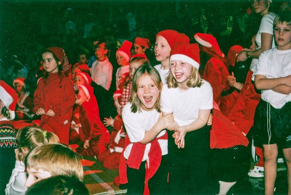 two young girls playing together at a party. they are both wearing red dresses and a 'nisse' (christmas elf) hat.