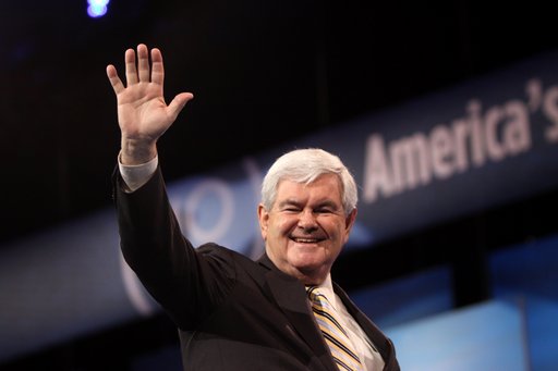 A photo of the American politician, historian, author and political consultant Newt Gingrich from the chest up. He is smiling and waving while looking down at the photographer.