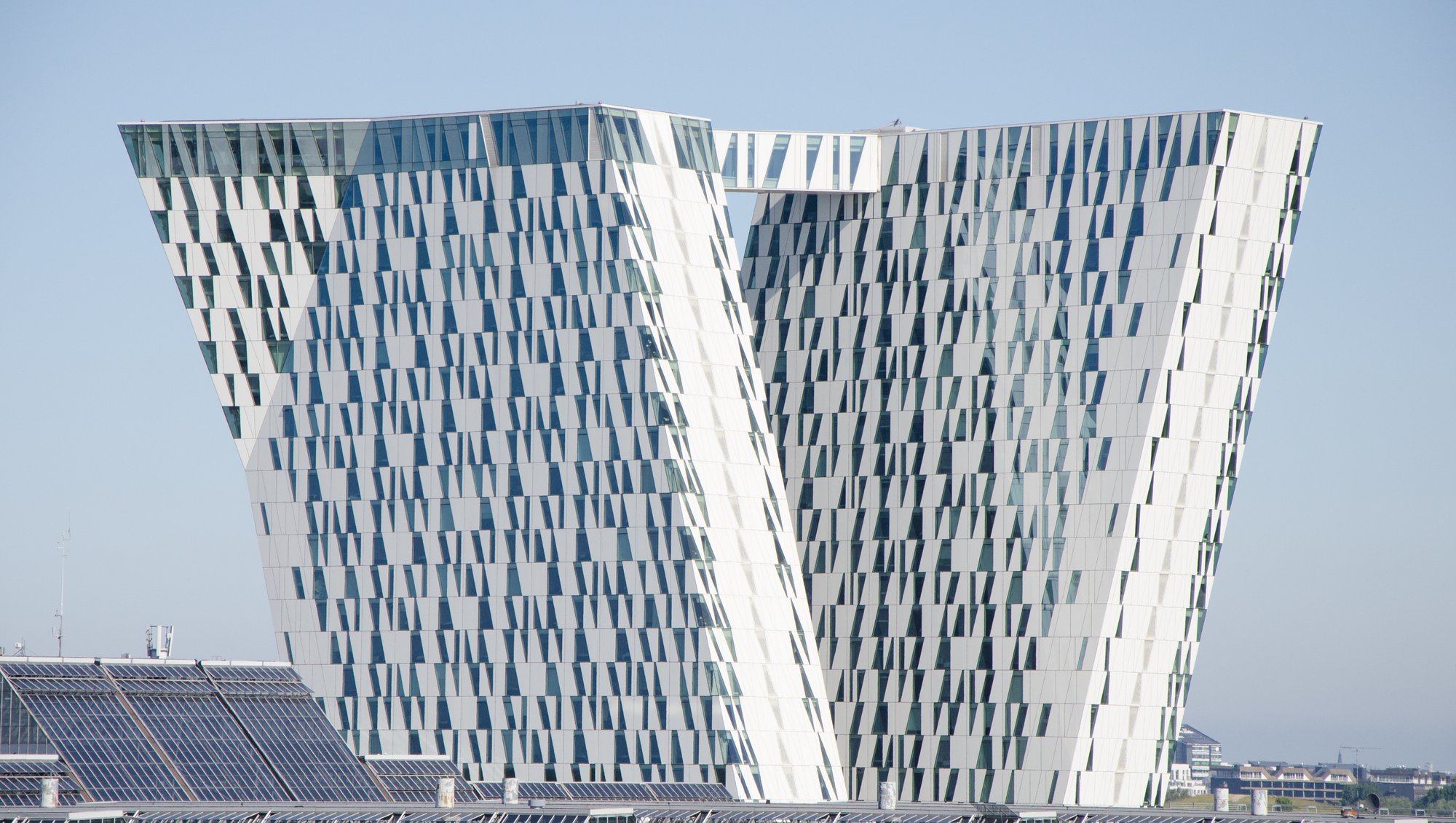 A powerful expressive work with two inclined and faceted towers connected by a sky bridge. The buildings are trapez shaped and made with white plates and glass