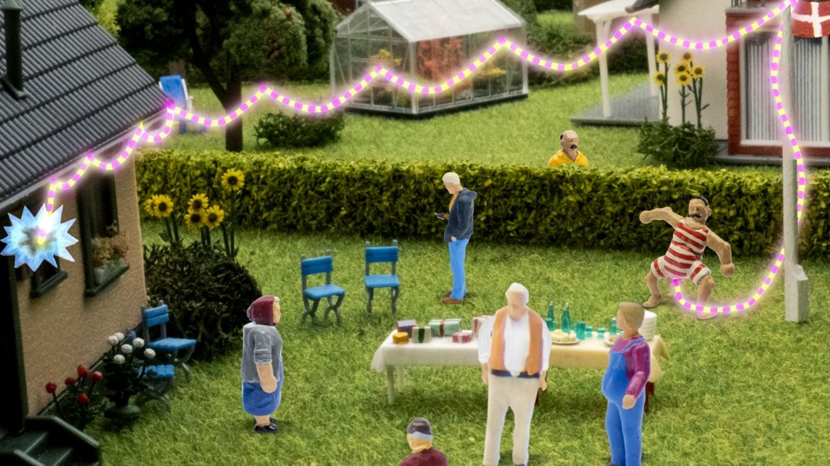 Pictured is a screenshot from an episode of the Danish TV show 'John Dillermand' (translated to John Willyman). The animated clay figured are standing in a garden. John is wearing his signature red and white striped bodysuit, and he is using his very long, also red and white striped, penis as a lightbulb-decoration to celebrate a birthday in the garden.