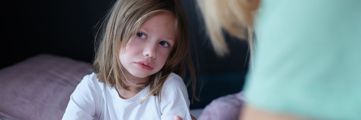 A picture of a young girl looking sad and pouty. In front of her, the shoulder of an adult can be seen.