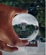 Upside down photo of a hand holding a glass ball. Through the glass ball, a green landscape and some houses are displayed, turned 180 degrees.