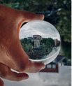 Upside down photo of a hand holding a glass ball. Through the glass ball, a green landscape and some houses are displayed, turned 180 degrees.