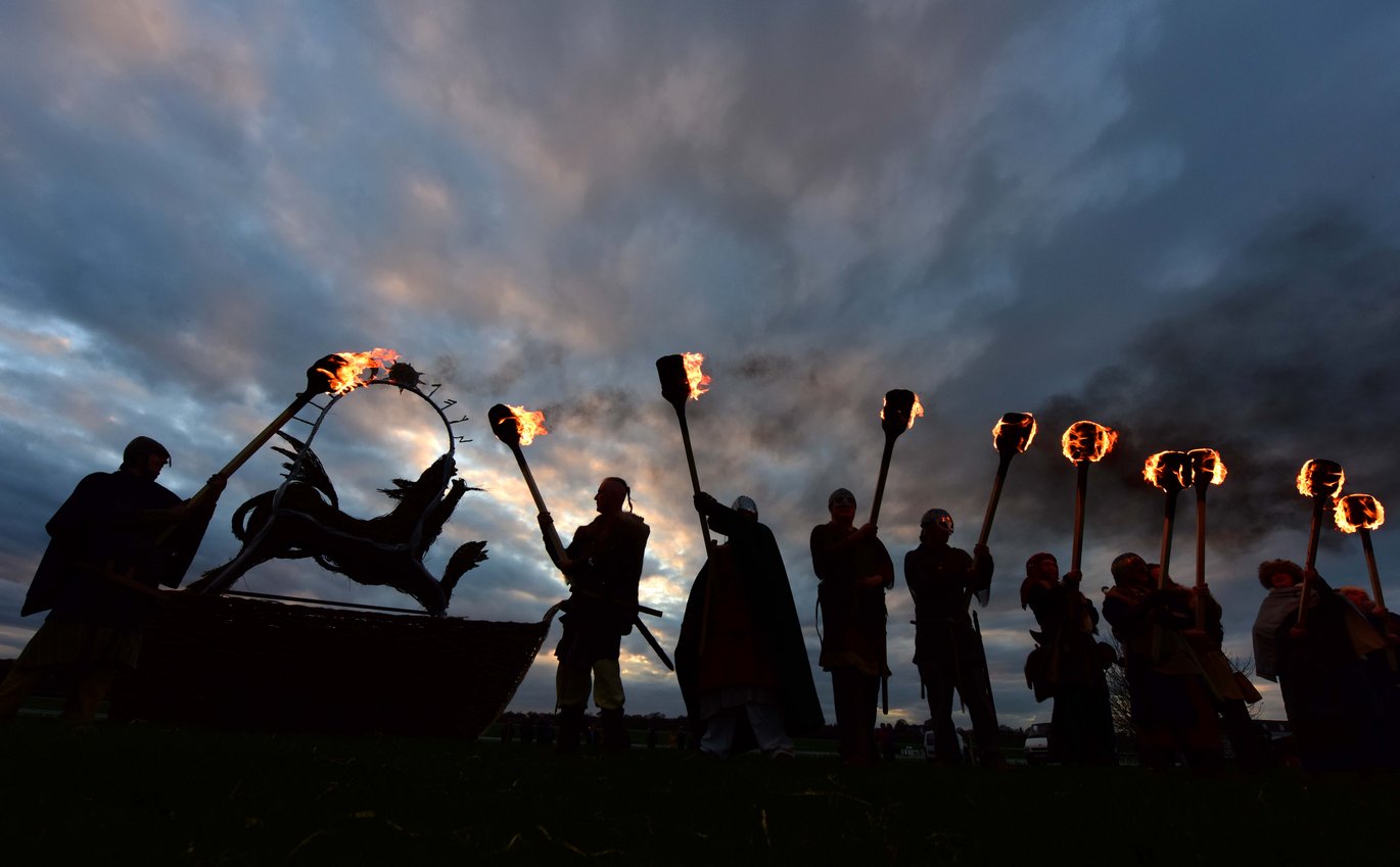 Dark hillside with men in Viking costume with torches