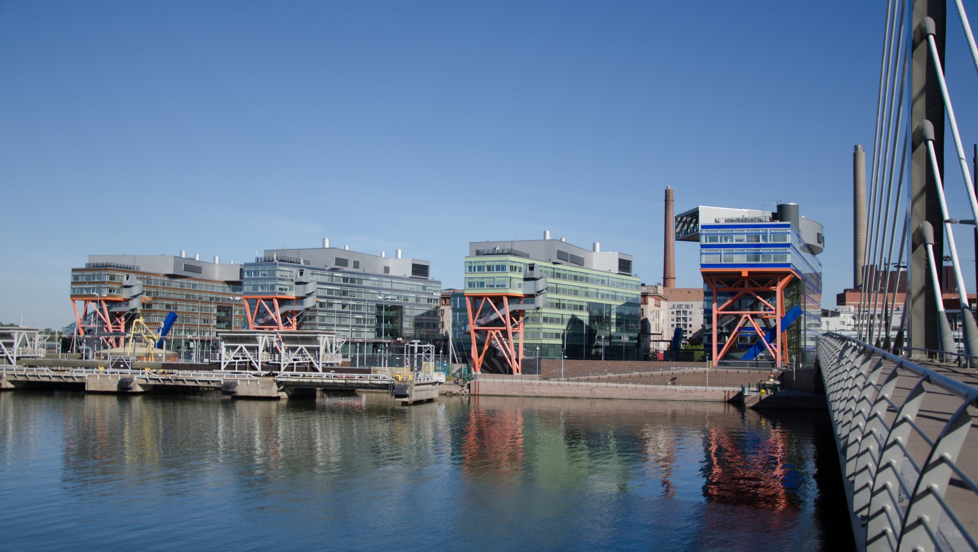 Four buildings covered with glass windows placed right beside each other very close to the habour. They each have a crane-like structure in the front. That means - poles geometrically structured across each other for a strong hold.