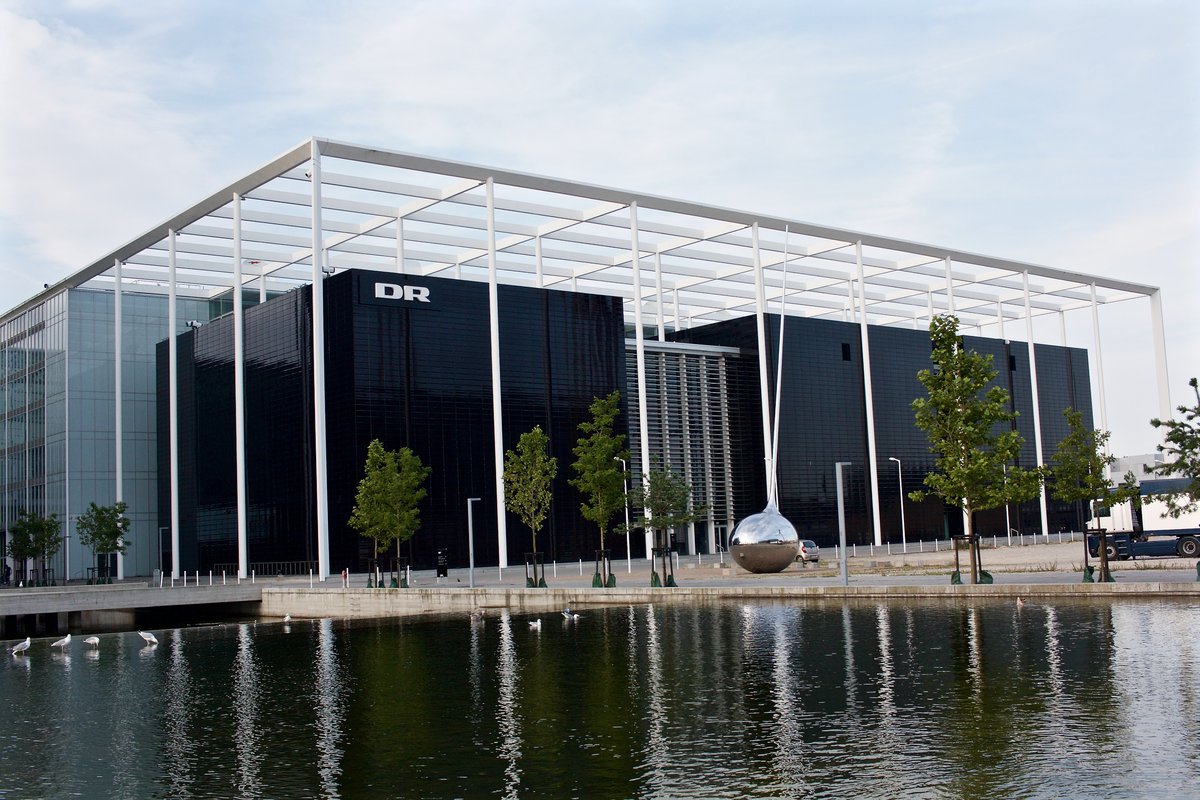A large black glass square building with the logo of DR on its corner