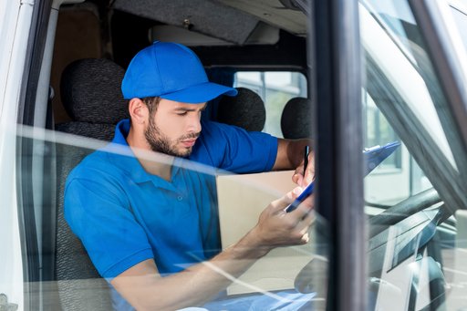man sitting in a car wearing work clothes and a cap, looking at his phone