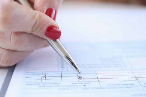 A picture of a hand wearing red nail polish filling out a questionnaire on paper with a ballpoint-pen.