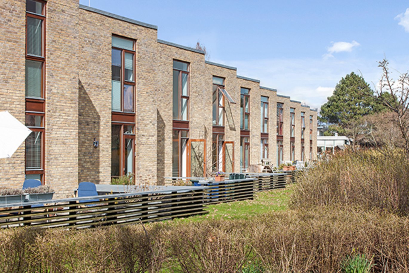 A row of modern, brown-brick terrace houses with small front gardens in daylight.