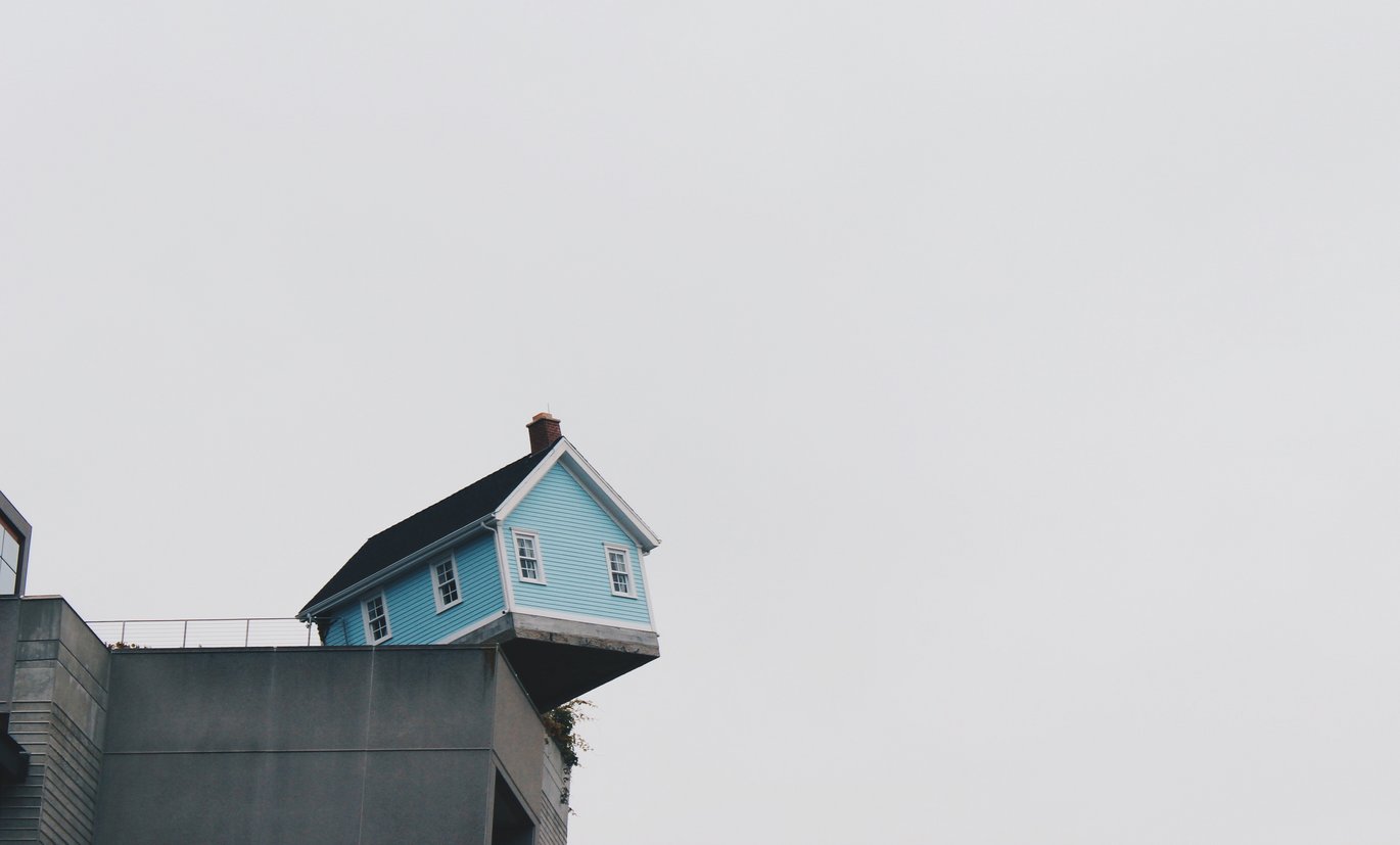 Small, blue wooden house balancing on a modern building.