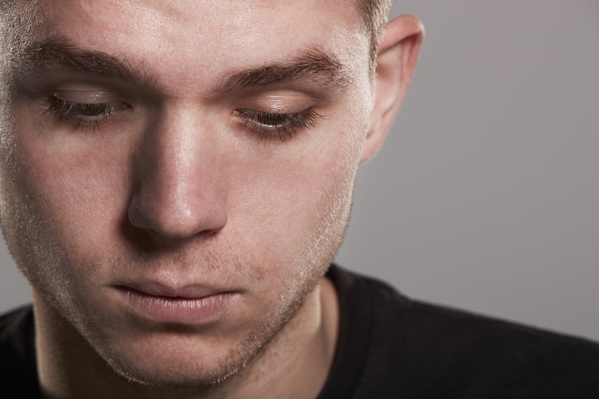 A close-up picture of a man looking downwards with a sad and ashamed expression on his face.