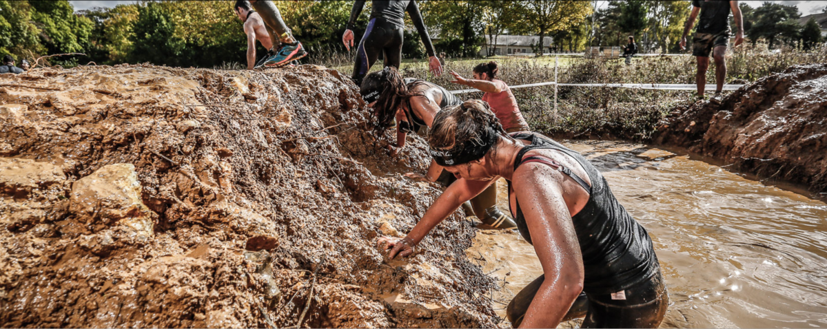 A picture of three women trying to climb their way out of a mud pool.