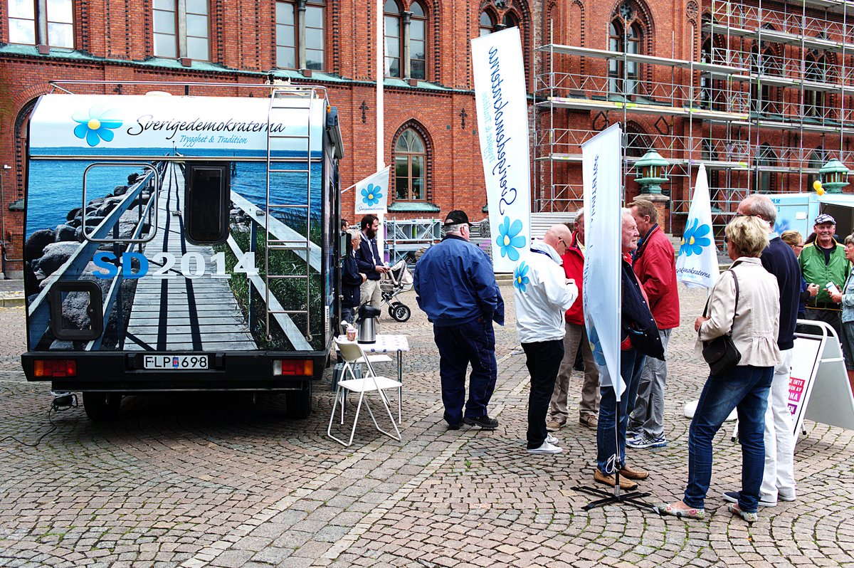 En gruppe af ældre mænd tilhørende partiet Sverigedemokraterne fører valgkampagne på en gågade. De har en malet campignvogn med.