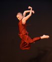 Dancer dressed in maroon silk with arms and legs behind them while they jump in the air