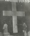 Hazy, old picture of a ship being painted with a large white cross.
