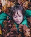 Child surrounded with a bunch of autumn leaves