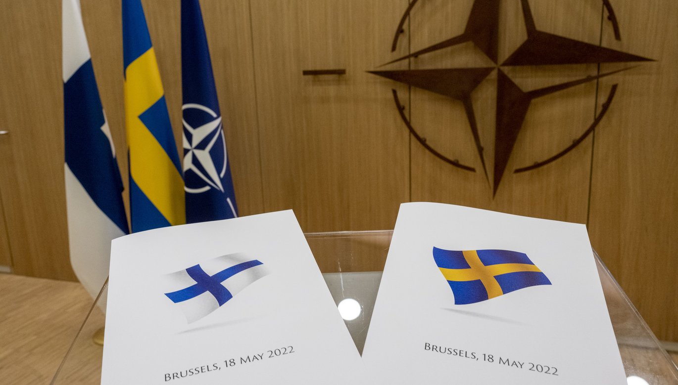 Two documents, one with the Finnish flag and one with the Swedish flag, laying on a glass table in an official-looking office.