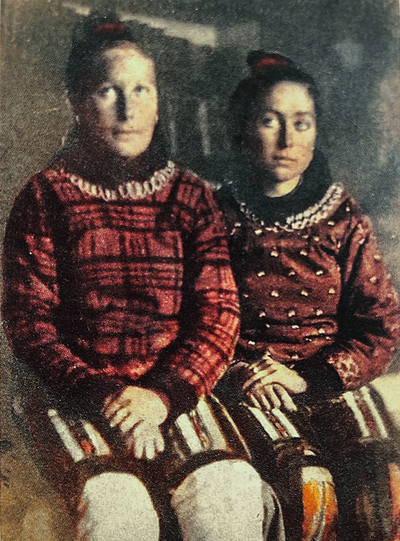 Old photo of two girls sitting beside each other in long red dresses with pattern