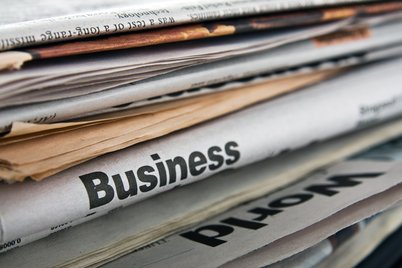 A stack of primarily business newspapers, the titles of which are obscured.
