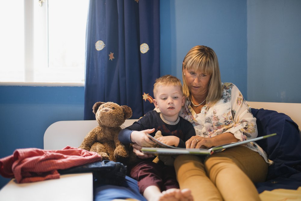 a mom and her son sitting on a bed reading a children's book