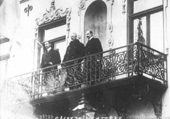 Black and white photo of three men (Kings) standing beside each other on a balcony and looking out, presumably towards the audience