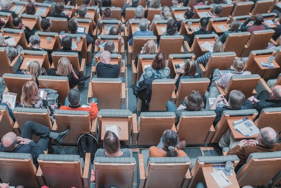 lots of people sitting beside each other on rows, looks like inside a parliament